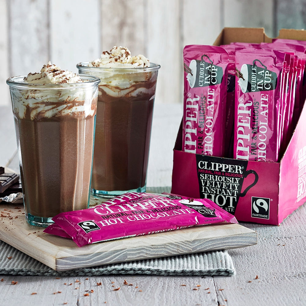 Clipper Hot Chocolate Sachets in a box next to two tall glasses of hot chocolate topped with whipped cream